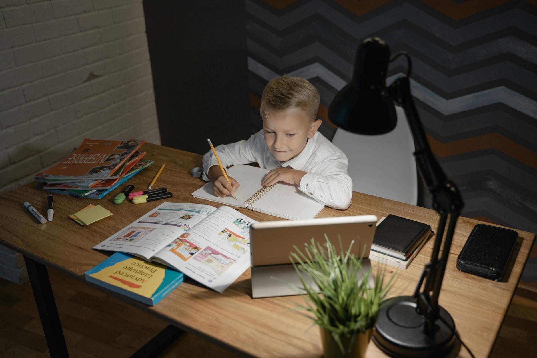 Chłopiec uczy się przy drewnianym biurku z tabletem i książkami