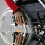 Dłoń użytkownika na kole wózka inwalidzkiego odbijająca się w szybie