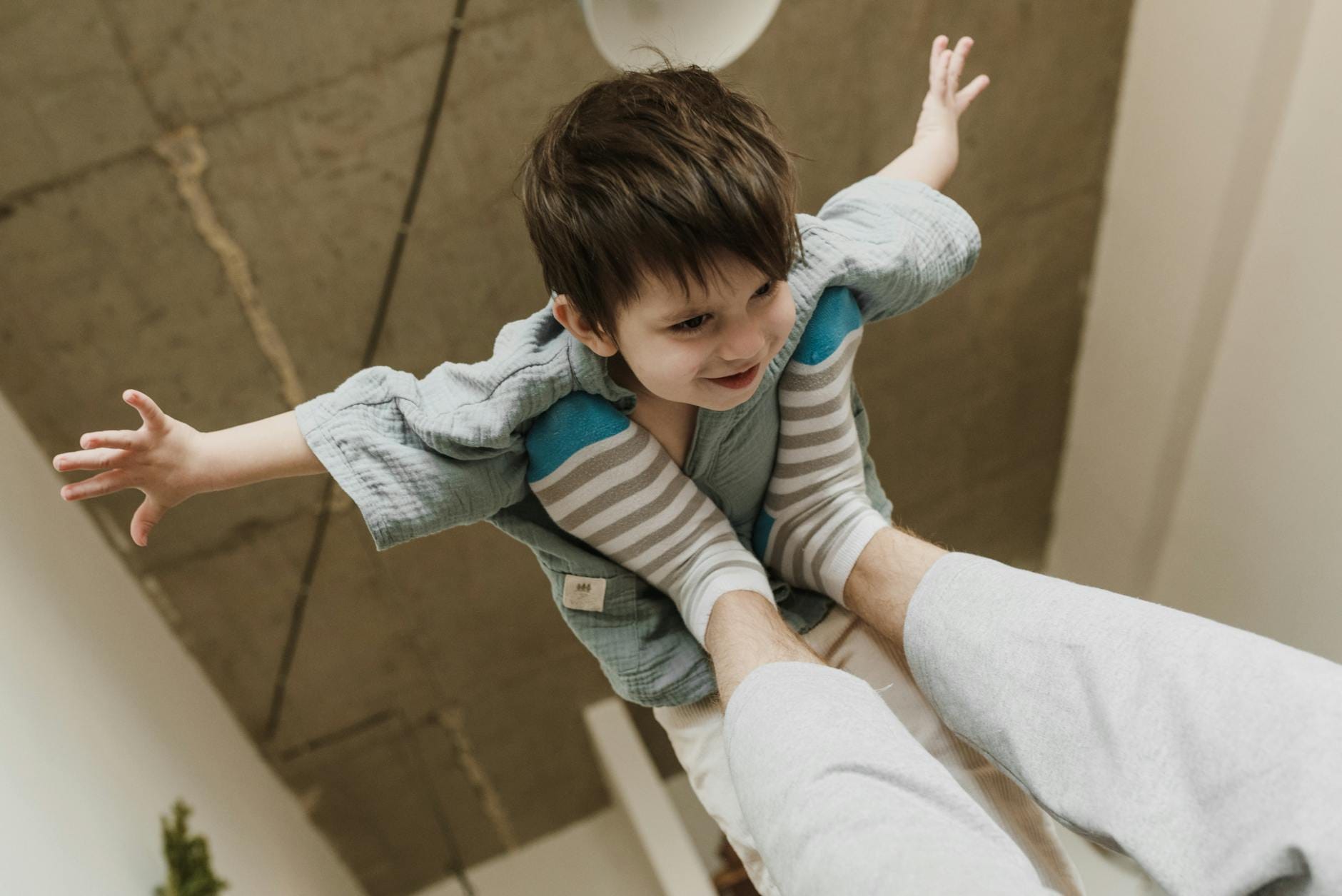 Dziecko unoszone stopami dorosłego bawi się w samolot w salonie