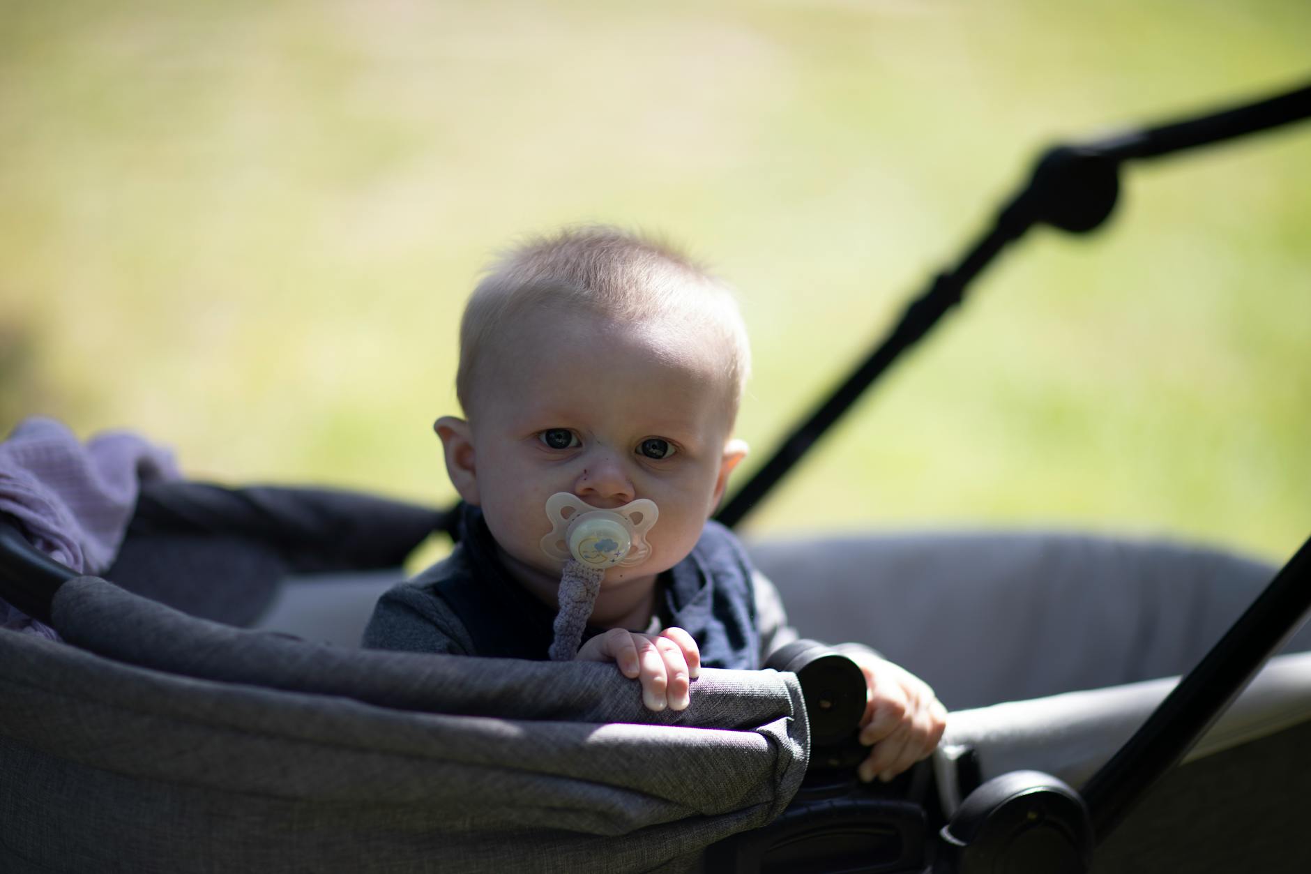 Niemowlę w spacerówce z smoczkiem podczas słonecznego spaceru w parku