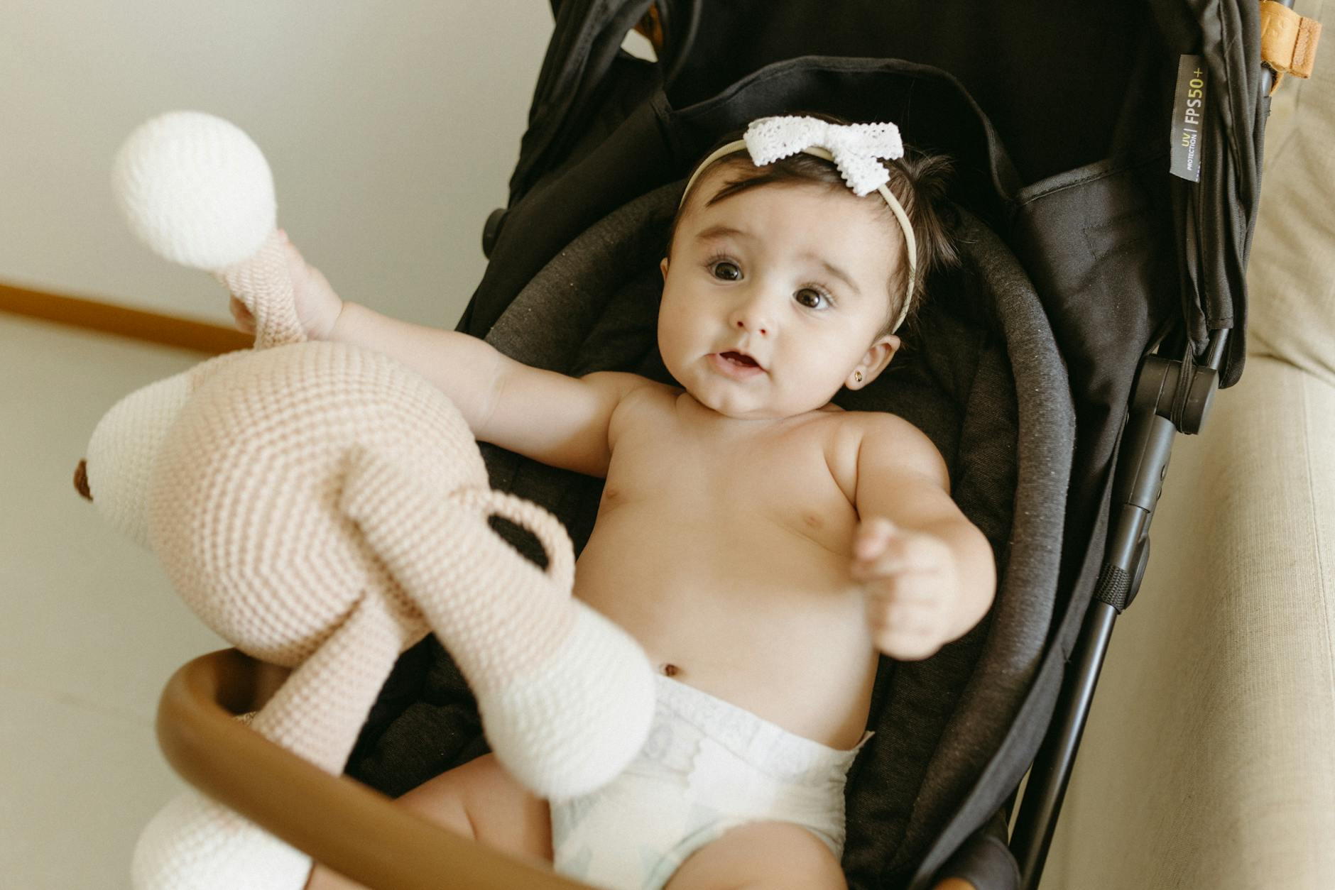 Uśmiechnięta dziewczynka w wózku trzymająca szydełkową zabawkę