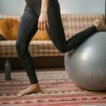 Kobieta w czarnych legginsach ćwiczy równowagę w domu na piłce fitness