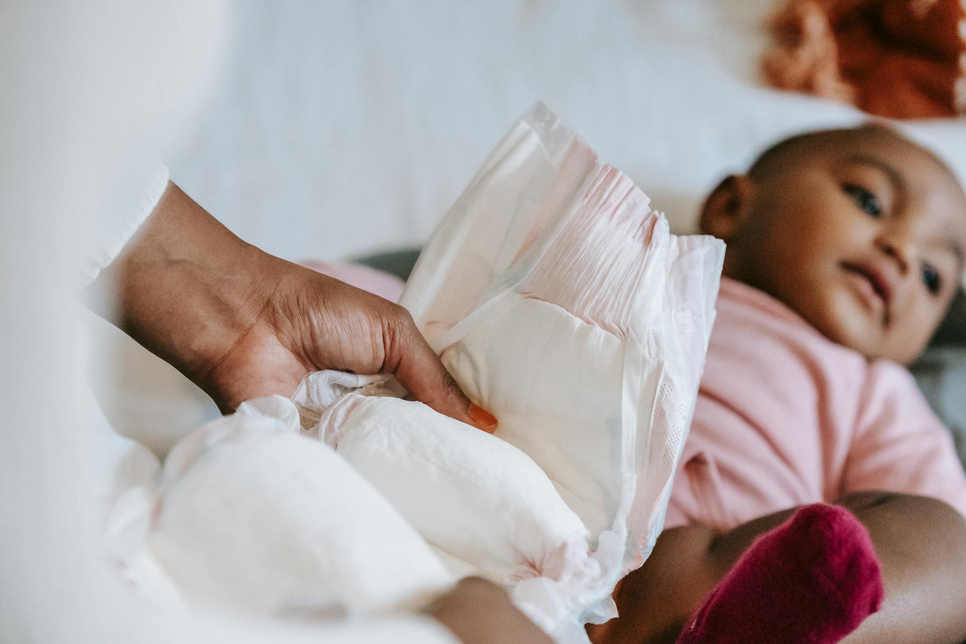 Mama przewija niemowlę na przewijaku, stojąc z boku dla asekuracji